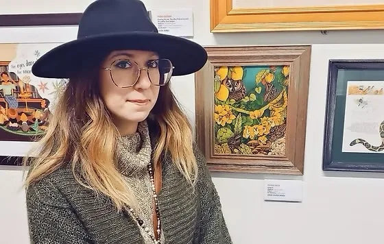 Artist Angela Rizza standing beside her framed artwork